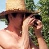 andrew david harkey on the beach holding a camera in hand, forest in the background